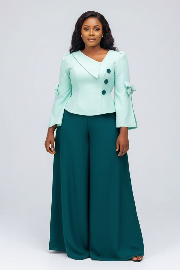 Woman wearing a light green blazer and teal pants on a white background