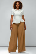 Woman wearing a white peplum top and tan wide-leg pants on a gray background